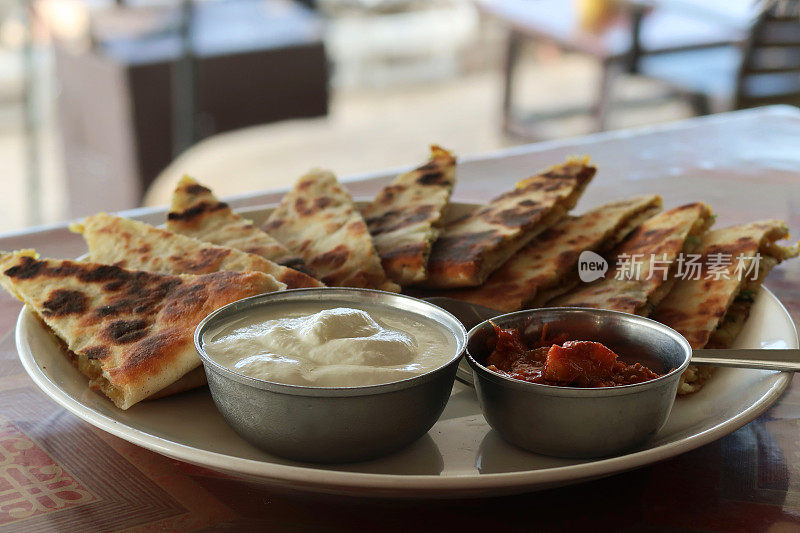 这是印度自助早餐的特写，白色的盘子上放着三角形的aloo paratha切片，上面撒着焦糖洋葱，美味的面包里塞满了garam masala土豆，酒店餐厅aloo paratha菜，raita凝乳酸奶